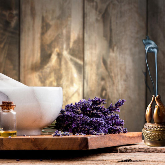 a wooden table with a white bowl, a vase of purple flowers, and a small glass bottle with a cork stopper.